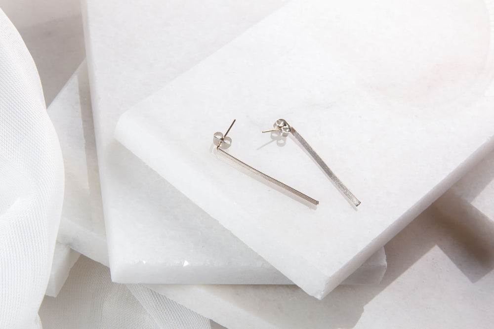 Two silver bar earrings made out of guitar strings on a layered white background