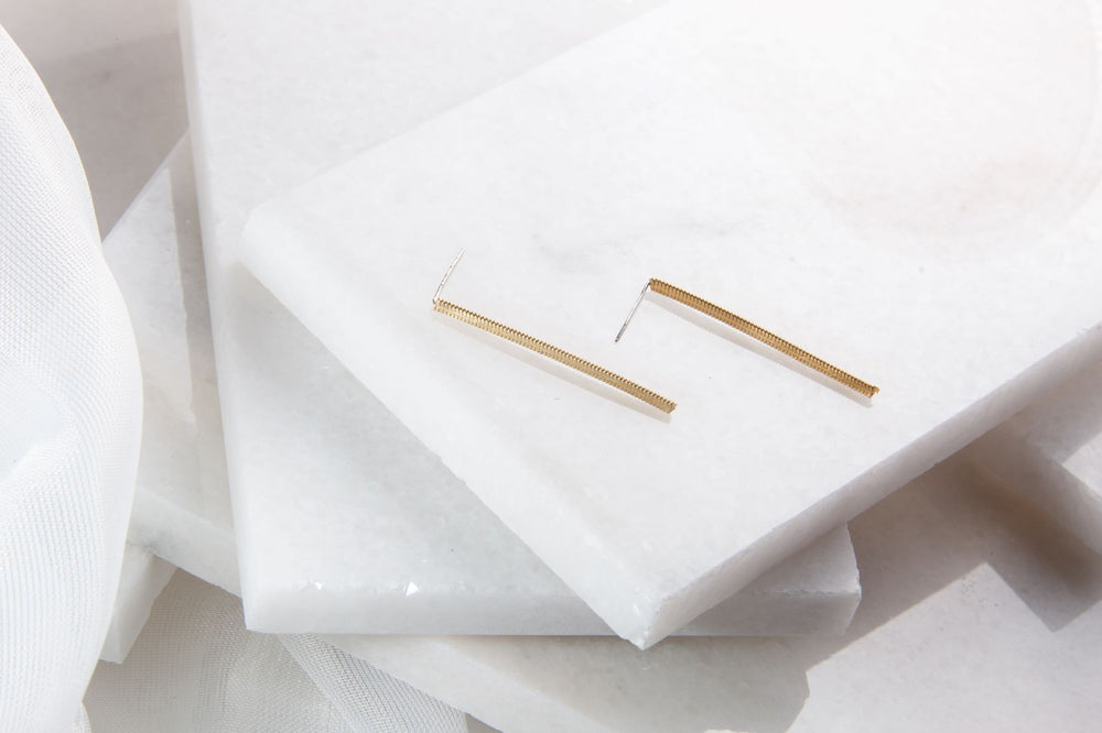 Two gold bar earrings made out of guitar strings on a layered white background