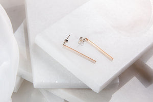Two rose gold plated bar earrings made out of guitar strings on a layered white background