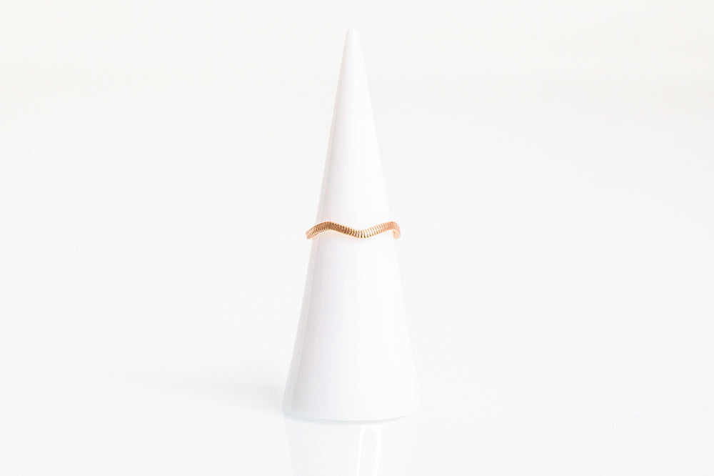 A flattened guitar string ring. Plated in 14k rose gold, wavy shape, string texture