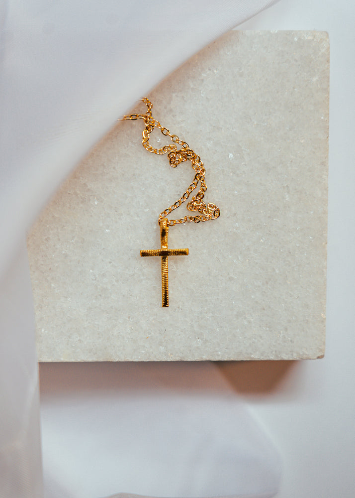 gold cross pendant on a gold chain laying on white marble