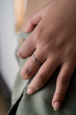 A women's hand modeling a flattened guitar string ring. Stainless steel. , wavy shape, string texture